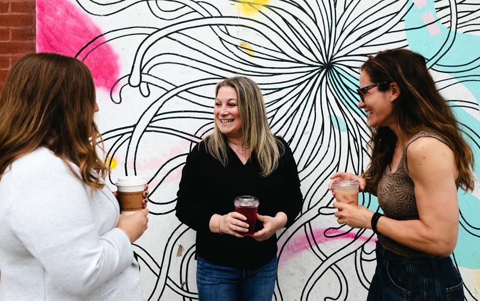 Julie A. Katz laughing with two colleagues in front of a black and white mural
