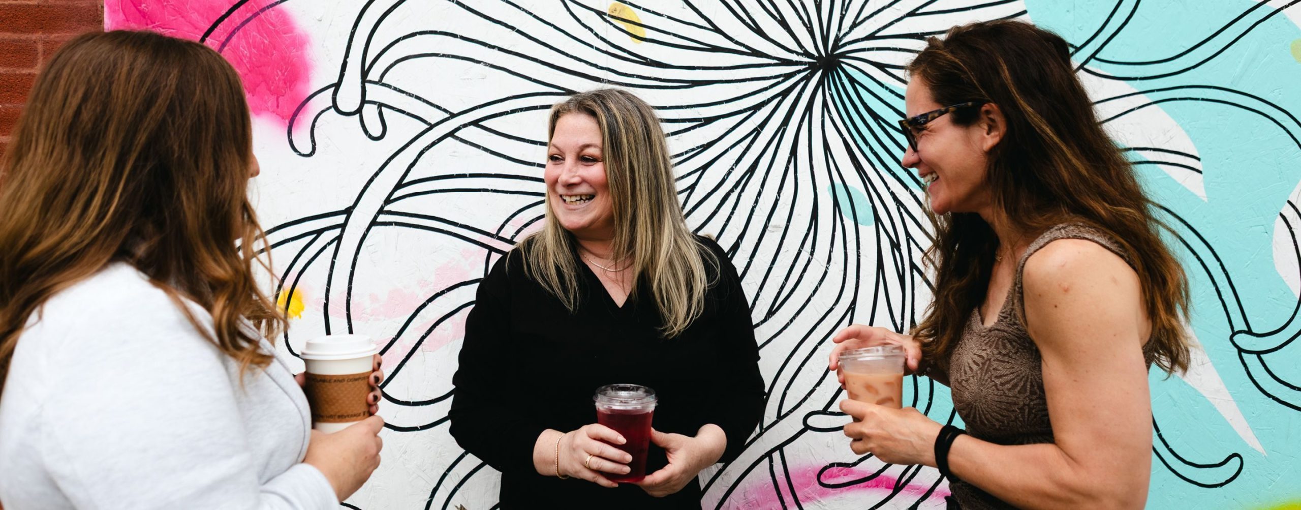 Julie A. Katz laughing with two colleagues in front of a black and white mural
