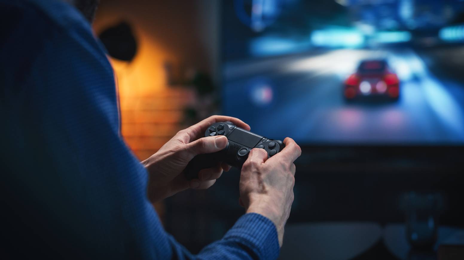 Man holding a game controller in front of a TV showing a racing game