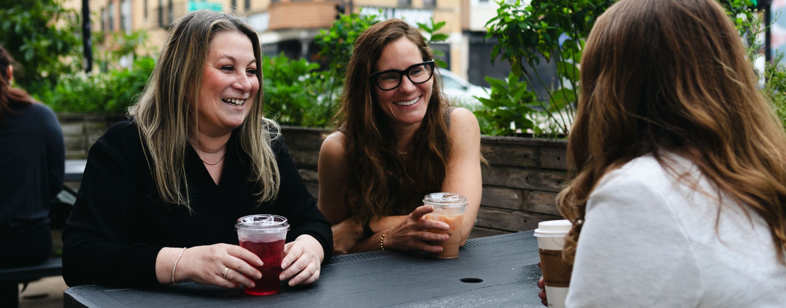 Three women talking at an outdoor café table with iced drinks