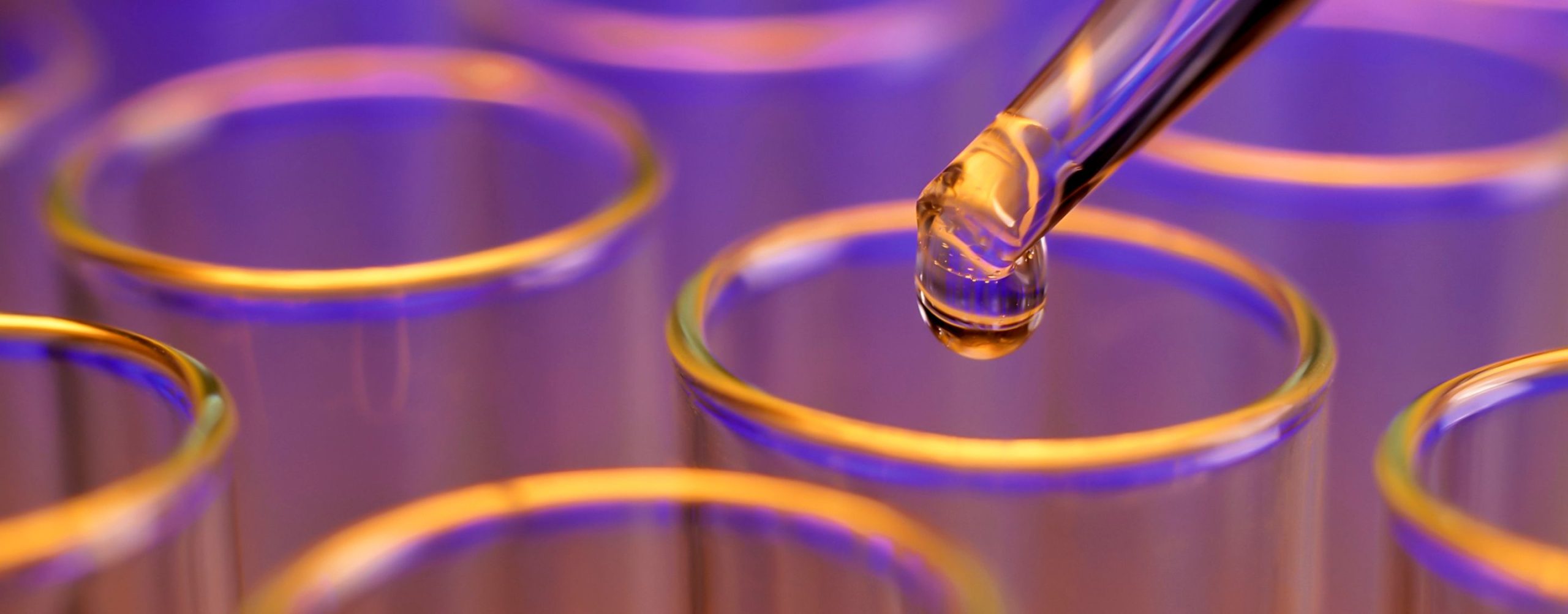 Pipette dripping liquid into glass test tubes under purple light